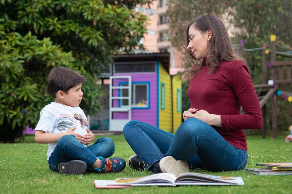 Alexandra Páramo conversa con un niño sentados frente a frente en el jardín