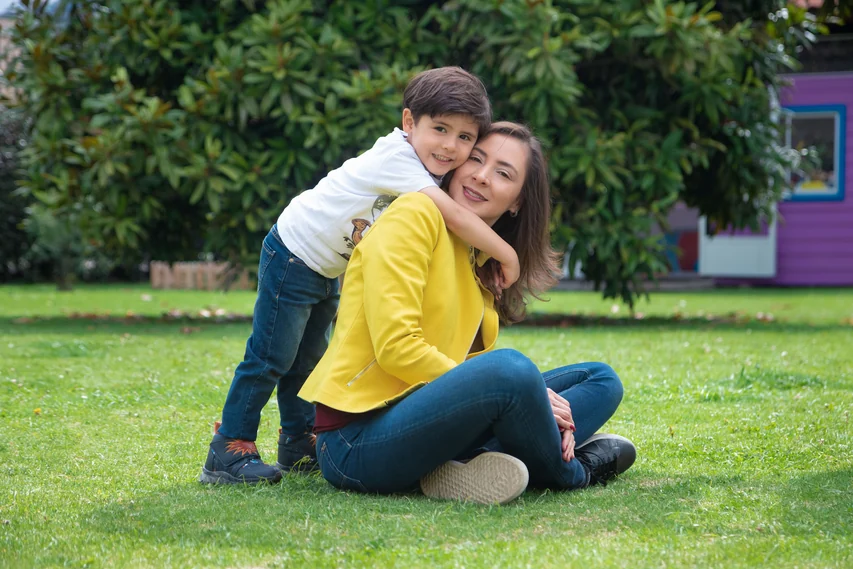 Alexandra Páramo sitting on the grass with a child hugging her from behind