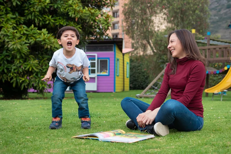 A child jumping next to Alexandra Páramo and an open storybook on the grass