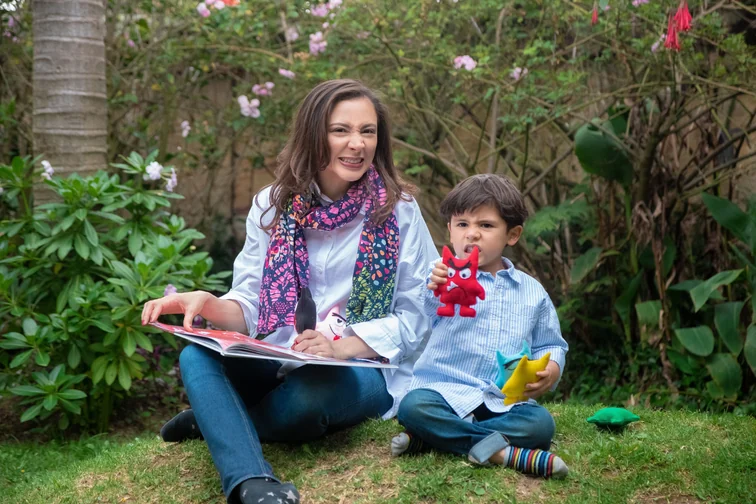 Alexandra Páramo with a child, an open storybook and colorful figures in the garden